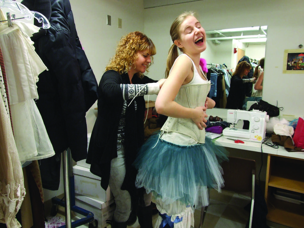 Griffin Reed struggles to put on her corset with the help of the costume director. [Makenna Martin]