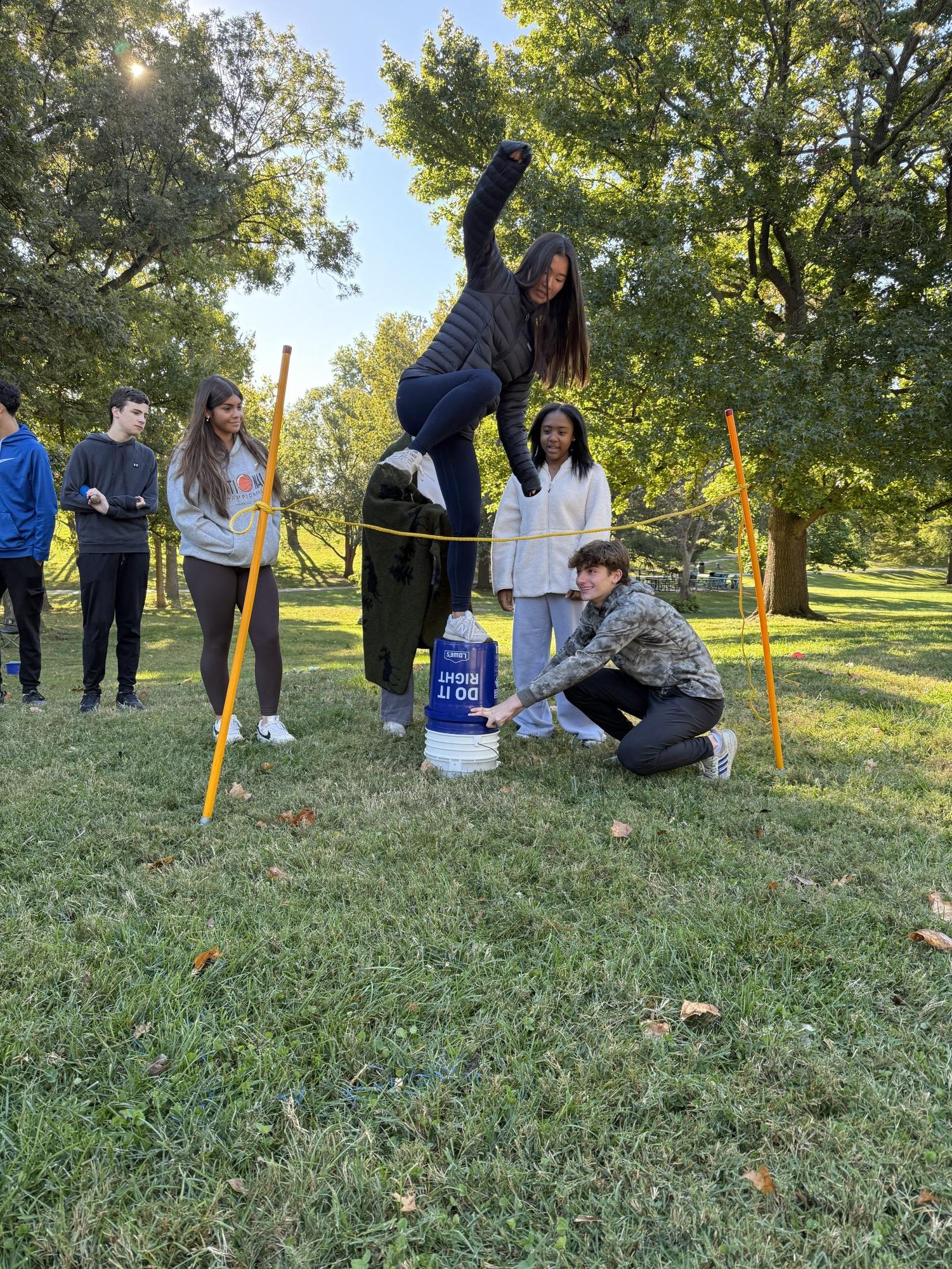 The sophomore class gathered at Shaw Park to participate in the sophomore challenge. Throughout the day, students rotated through team-building stations run by seniors. In this station, the rope represented an “electric fence,” and the sophomores had to find a way to get over the fence without touching it. Sophomore Lydia Lee balances on buckets to get over the obstacle.