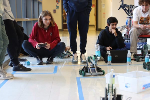 Senior Kian Eghtesady uses a remote control to drive vehicles for a Principles of Engineering project on Tuesday, Nov. 26. Sophomores Agastya Diwan and Karl HenkeCilenti watch. “I enjoy how hands-on the class is. It's really fun to design, build, and execute solutions for different problems and prompts such as a piston to crush a soda can,” Eghtesady said. “There's no one way to address a prompt, so I have the freedom to tackle it whatever way I think is best and adapt my solution based on the results.”